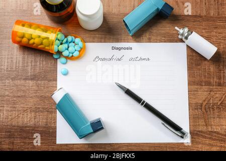Asthma inhalers, pills, pen and diagnosis form on wooden table Stock Photo