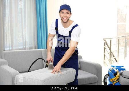 Dry cleaner's employee removing dirt from furniture in flat Stock Photo