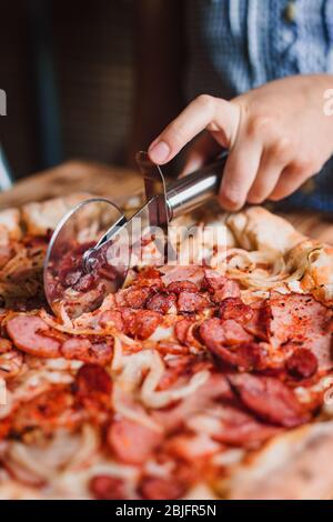 Cutting pizza on slices with special knife. Hand holding knife. Stock Photo