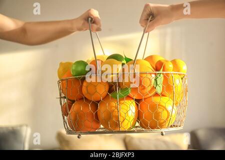 Hands of couple holding metal basket full of citrus fruits, indoors Stock Photo