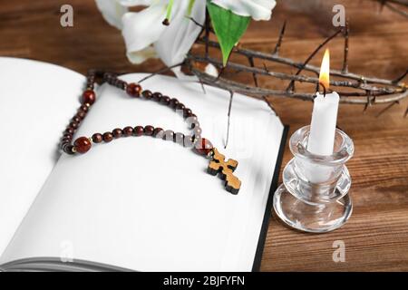 Opened blank book, candle with holder, rosary and crown of thorns on wooden table Stock Photo