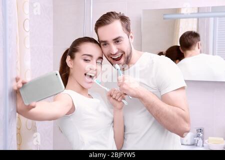Young happy couple taking selfie while brushing teeth in bathroom Stock Photo