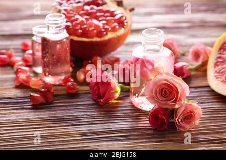 Perfume bottles, roses and pomegranate on wooden table Stock Photo