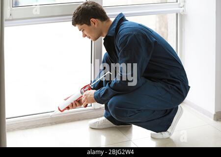 Young worker sealing joints of office window Stock Photo