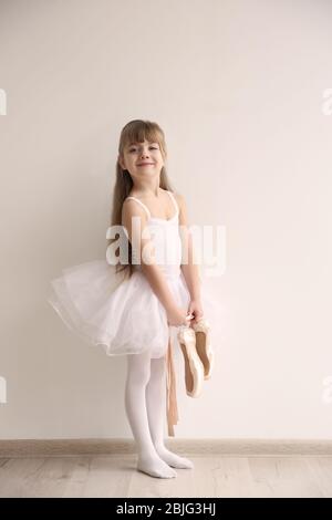 Beautiful little ballerina holding ballet shoes in light dance