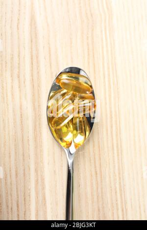Spoon with fish oil capsules on wooden table Stock Photo