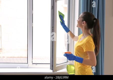 Young woman using detergent and rag while cleaning window in room Stock Photo