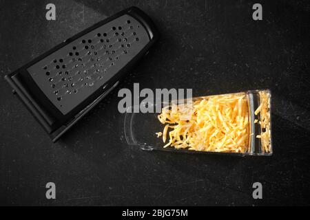 Plastic container with cheese and grater on table Stock Photo