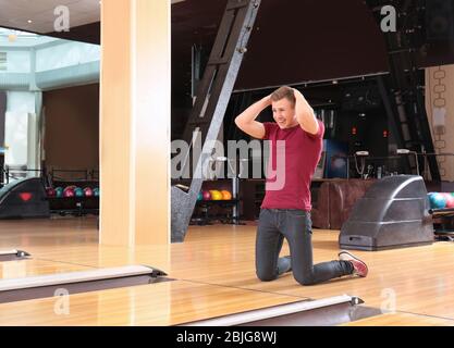 Upset young man standing on knees in bowling club Stock Photo