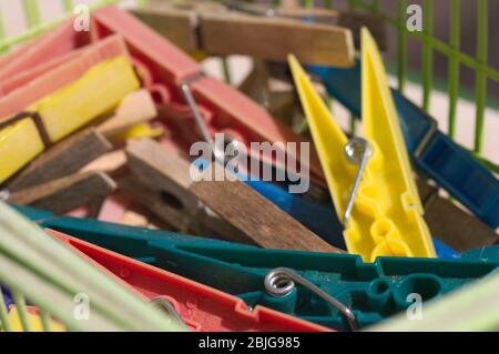 Multi-colored plastic clothespins mixed together with other wooden clothespins in a green basket Stock Photo