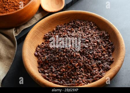 Cocoa nibs in wooden bowl on grey table Stock Photo