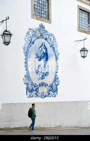 Young man passing blue and white azulejos ceramic tiles of Convent Church of Carmo in Guimares in Northern Portugal Stock Photo