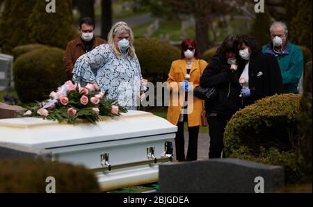 Everett, Massachusetts, USA. 28th Apr, 2020. The COVID-19, Corona Virus in Massachusetts is the third worst hit state in America. The Woodlawn Cemetery in Everett, MA is doing 3x the normal amount of funerals. Family in masks and gloves grieves before lowering the casket. Credit: Allison Dinner/ZUMA Wire/Alamy Live News Stock Photo