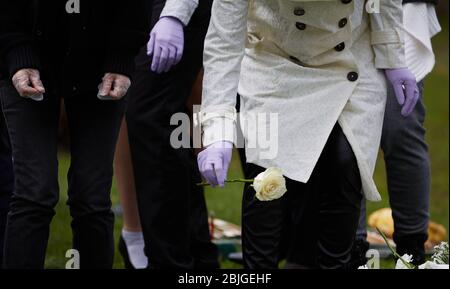 Everett, Massachusetts, USA. 28th Apr, 2020. The COVID-19, Corona Virus in Massachusetts is the third worst hit state in America. The Woodlawn Cemetery in Everett, MA is doing 3x the normal amount of funerals. Family members in gloves place flowers on a grave. Credit: Allison Dinner/ZUMA Wire/Alamy Live News Stock Photo