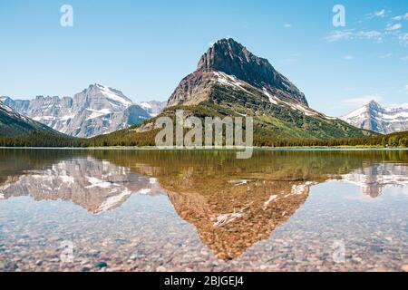 A snowy mountain water reflection on Swiftcurrent Lake in Many Glacier region of Glacier National Park, Montana. Grinnell Point, a subpeak of Mount Gr Stock Photo
