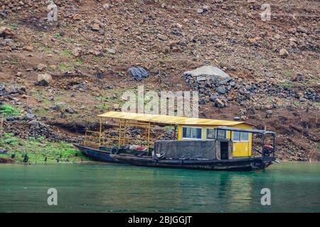 Wuchan, China - May 7, 2010: Dragon Gate Gorge on Daning River. Closeup of Black local ferry at yellow floating hop-on, hop-off pier on emerald green Stock Photo