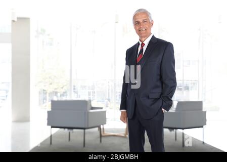 Portrait of a smiling mature businessman standing in a modern building lobby. Vertical format with High Key background. Stock Photo