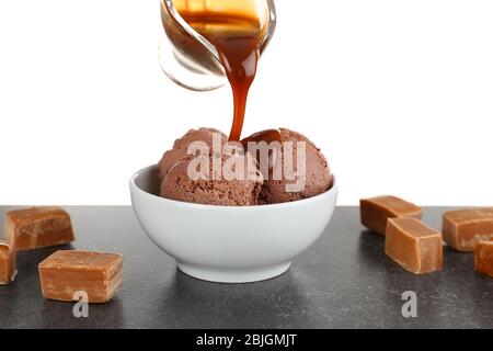 Pouring caramel sauce onto chocolate ice cream in bowl against white background Stock Photo