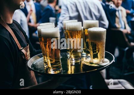 waiter carries tray full of glasses of beer to customers at outdoor bar or pub Stock Photo