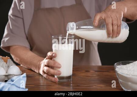 Old woman pouring fresh milk into glass on table Stock Photo