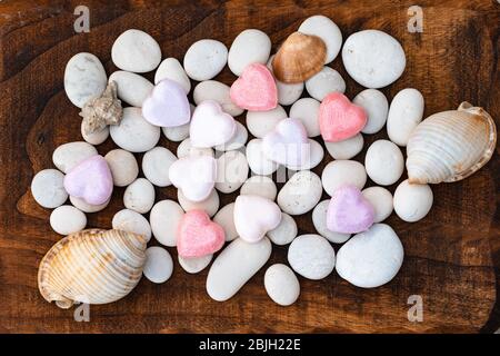 river stones left on a rough wooden board.a lonely heart on white stones.river stones left on a rough wooden board with hearths and seashells Stock Photo