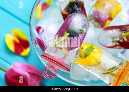 Homemade popsicles with flowers in glass bowl on blue wooden table Stock Photo
