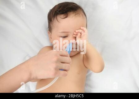 Mother using nasal aspirator for cute little baby lying on bed at home. Health care concept Stock Photo