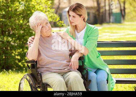 Disabled elderly woman and young caregiver in park on sunny day Stock Photo