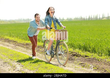Handsome young man teaching his girlfriend to ride bicycle in countryside Stock Photo