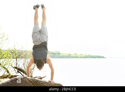 Young sporty man doing acrobatic exercises near river Stock Photo