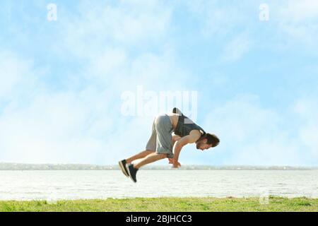 Young sporty man doing acrobatic exercises near river Stock Photo
