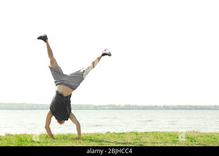 Young sporty man doing acrobatic exercises near river Stock Photo
