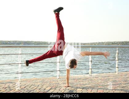 Young sporty man doing acrobatic exercises near river Stock Photo
