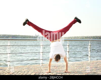 Young sporty man doing acrobatic exercises near river Stock Photo