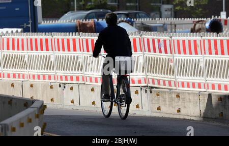Rostock, Germany. 28th Apr, 2020. A cyclist rides past a long site fence. The latest unemployment figures will be published on 30.04.2020. Credit: Bernd Wüstneck/dpa-Zentralbild/ZB/dpa/Alamy Live News Stock Photo