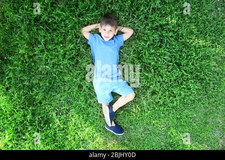Cute little boy lying on green grass in park Stock Photo