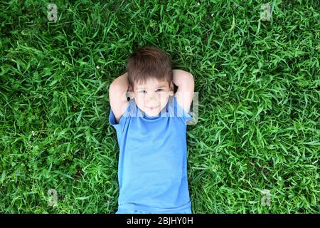 Cute little boy lying on green grass in park Stock Photo