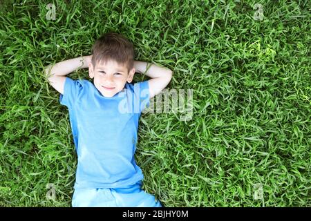 Cute little boy lying on green grass in park Stock Photo