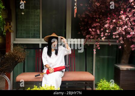 Travelers thai women wearing clothes vietnamese ethnic style with bamboo hat and red umbrella for take photo at garden and vintage retro house in reso Stock Photo