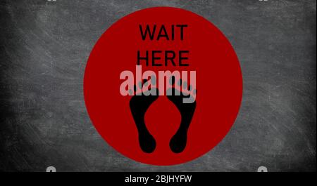 Social distancing sign at supermarket waiting circle for standing on distance in line at cash register. COVID-19 Coronavirus message to stay away from people. Red round with feet drawing and text. Stock Photo