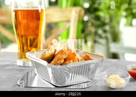 Foil container with tasty fried fish and chips on table Stock Photo
