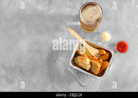 Foil container with tasty fried fish and chips on table Stock Photo