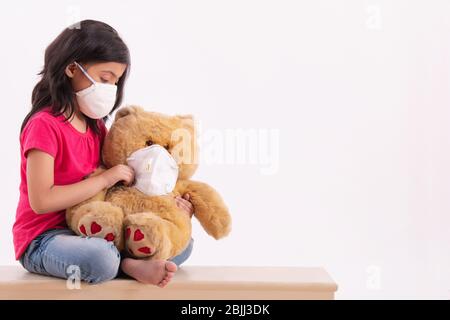 Young girl putting a pollution mask on her teddy bear as her due to terrible weather outside. (Children) Stock Photo