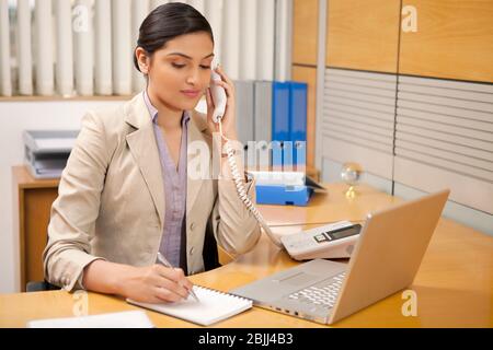 Female executive taking notes while on call Stock Photo