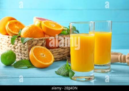 Composition with glasses of fresh juice and citrus fruits in wicker basket on table Stock Photo