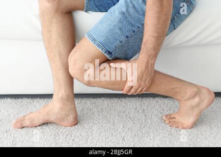 Young man suffering from leg pain at home Stock Photo