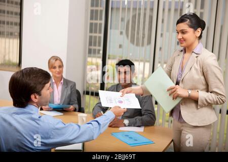 Businesswoman wearing formals passing document to businessman Stock Photo