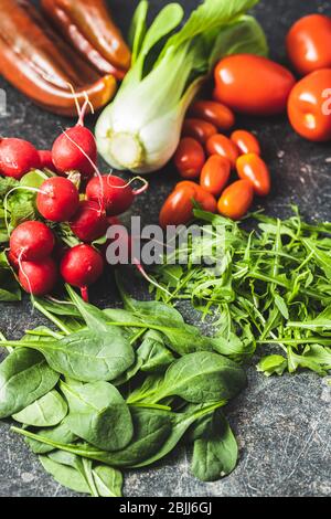 Different vegetables. Arugula, radishes, spinach, red peppers, tomatoes and pak choi on kitchen table. Stock Photo