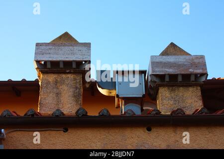 two chimneys and a drain outlet pipe on the cornice of an orange roof of a building Stock Photo