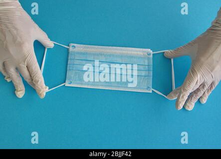 Hands in gloves holding medicine mask against the blue background Stock Photo